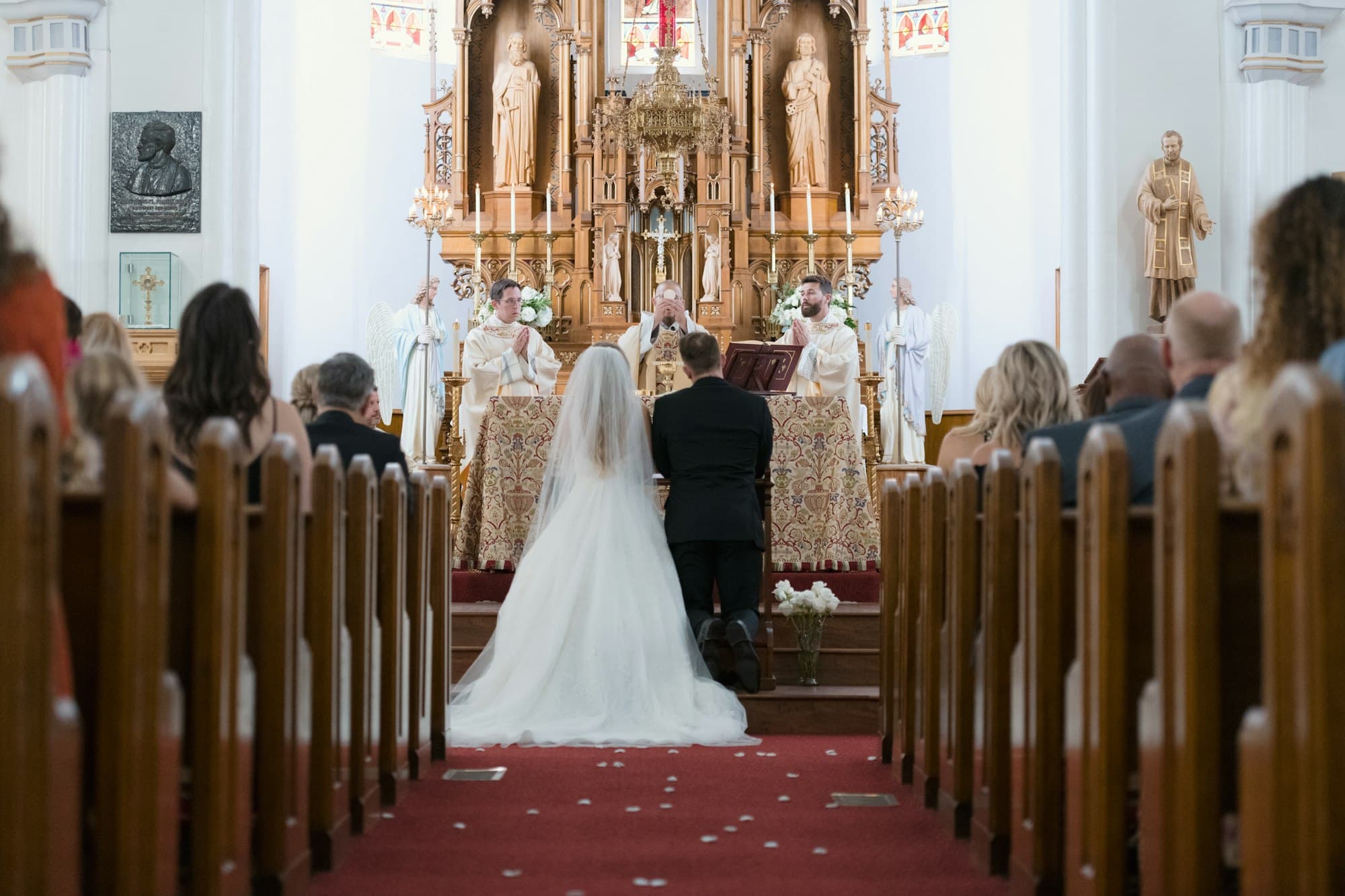 A bride and groom walk down the aisle of a church toward a gilded high altar
