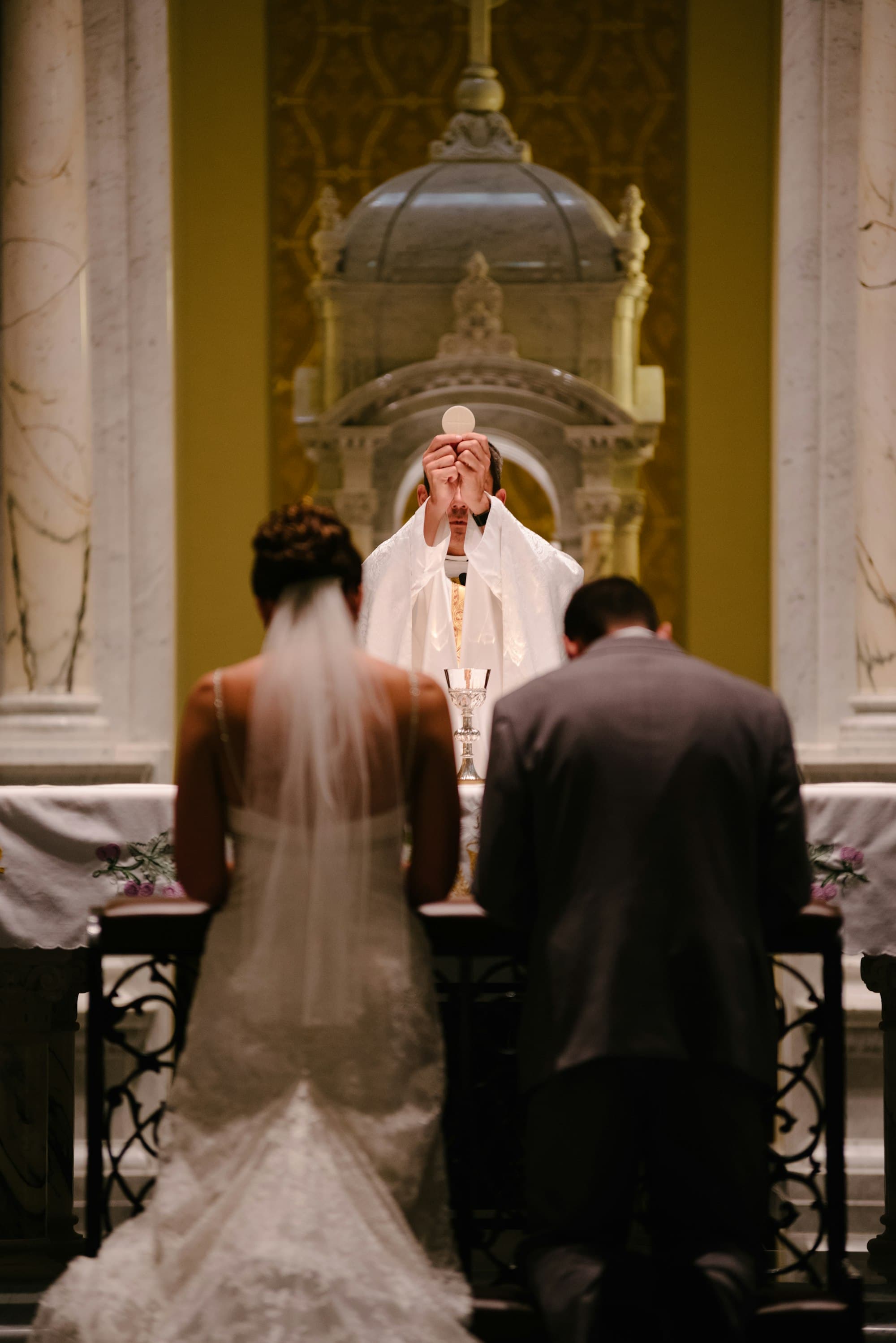 A couple kneels as the priest elevates the Host at the consecration