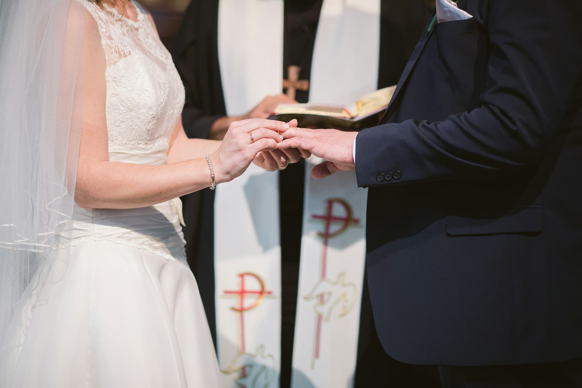 Bride and groom exchange rings beside a priest wearing a stole
